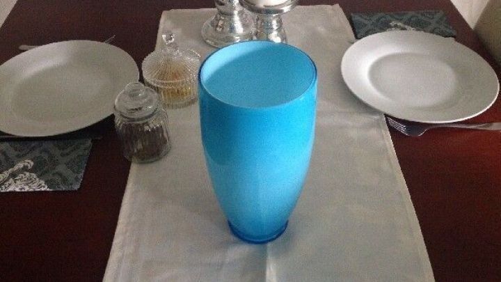 Eine blaue Vase steht als Tischabfallbeh&auml;lter auf einem Tisch, umgeben von Tellern und Kerzen, im Essbereich.