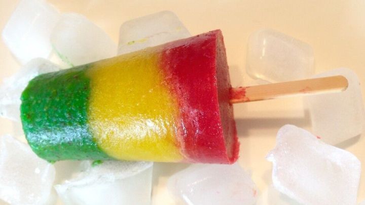 Ein buntes Smoothie-Eis auf einem St&auml;bchen liegt auf Eisw&uuml;rfeln und vermittelt ein erfrischendes Sommerfeeling.