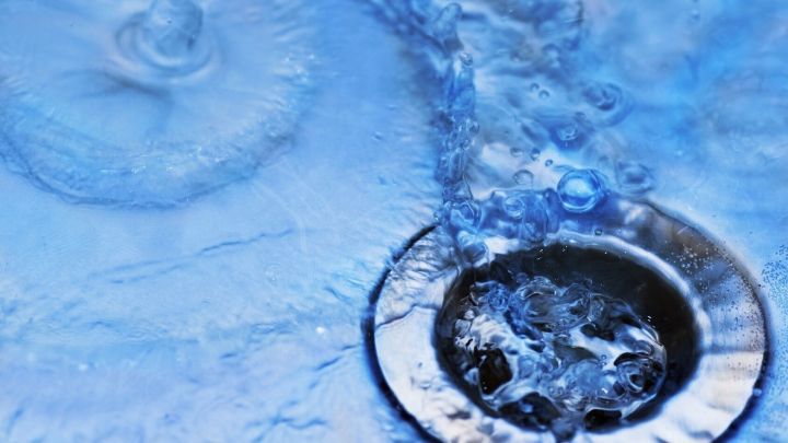 Wasser flie&szlig;t klar und sprudelnd in einen Abfluss, umgeben von einer blauen Oberfl&auml;che ohne Ablagerungen.