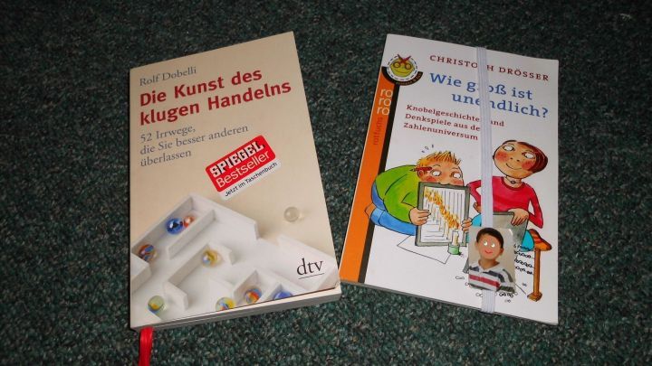 B&uuml;cher mit Leseb&auml;ndchen liegen auf einem dunklen Teppich, eins zeigt Anleitungen, das andere illustriert Kinderaktivit&auml;ten.