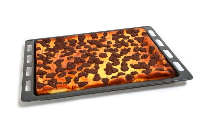 Ein Backblech mit einem bunten, gebackenen Kuchenbelag steht bereit, um zur&uuml;ckgebracht zu werden.