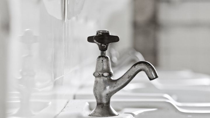 Ein veralteter Wasserhahn befindet sich an einem wei&szlig;en Waschbecken und vermittelt den Eindruck von seltener Nutzung.