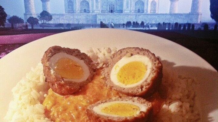 Saftige indische Hackb&auml;llchen mit Ei liegen auf duftendem Reis und werden von einer Joghurtso&szlig;e umgeben, im Hintergrund das Taj Mahal.