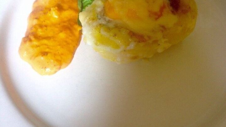 Ein gebratenes Ei mit einer gebackenen Kartoffel und einem frischen Basilikumblatt auf einem wei&szlig;en Teller serviert.