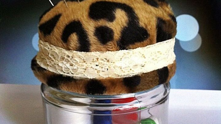 Ein Nadelkissen mit Aufbewahrung, dekoriert mit tierischem Muster, steht auf einem Glas voller N&auml;hutensilien und macht Ordnung.