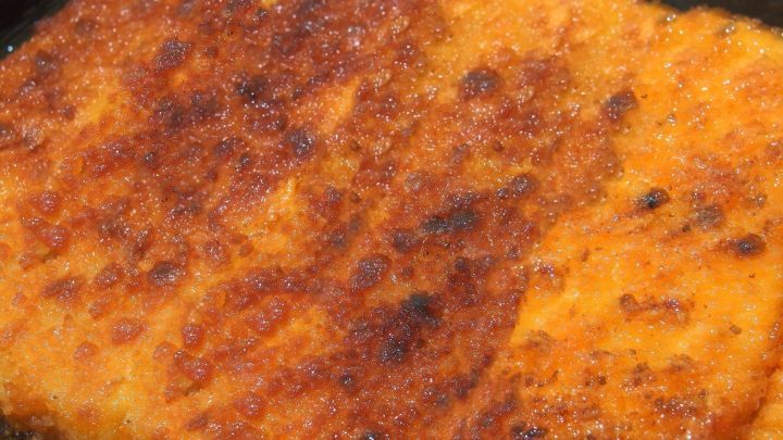 Knusprige Scheibe mit goldbrauner Panade aus St&auml;rkemehl, frisch aus der Pfanne, umgeben von dunklem Kochgeschirr.