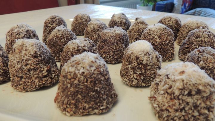 Schokobomben liegen eng beieinander auf einem Teller, &uuml;berzogen mit geraspelten Kokosflocken auf einem Tisch.