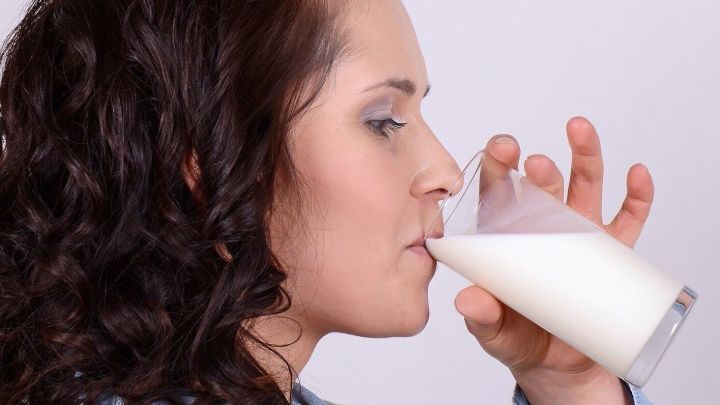 Eine Frau trinkt Magermilch aus einem Glas und genie&szlig;t das gesunde Getr&auml;nk in einem neutralen Hintergrund.