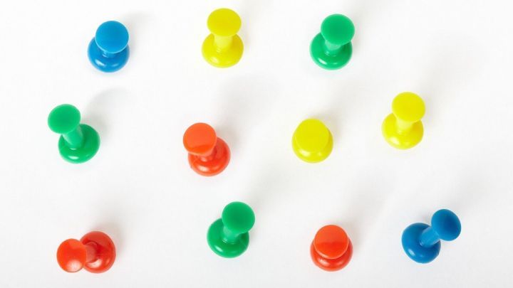 Bunte Rei&szlig;n&auml;gel liegen verstreut auf einer wei&szlig;en Fl&auml;che, bereit zum Befestigen von Notizen an der Wand.