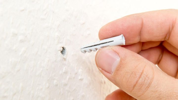 Ein D&uuml;bel wird in ein Loch in einer wei&szlig;en Wand eingef&uuml;hrt, w&auml;hrend eine Hand ihn h&auml;lt, um ihn korrekt zu positionieren.