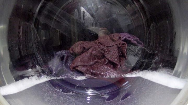 Im Inneren einer Waschmaschine liegt ein lila Kleidungsst&uuml;ck, w&auml;hrend Seifenblasen aufsteigen und Wasser sprudelt.