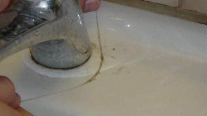 Zahnseide wird verwendet, um Schmutz um einen Wasserhahn auf einem Waschbecken zu entfernen.