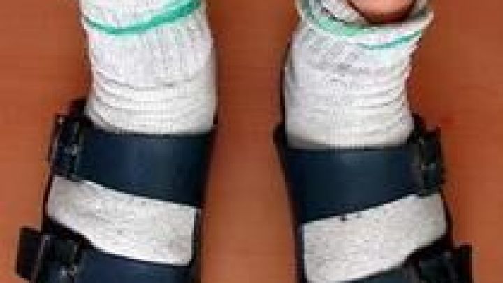 Wei&szlig;e Socken stecken in offenen Sandalen, w&auml;hrend der Tr&auml;ger auf einem Holzfu&szlig;boden steht. Ein Beispiel f&uuml;r Socken-Stil.