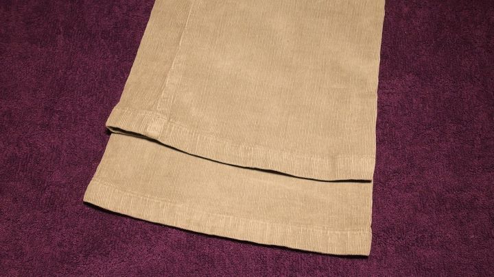 Ein Paar beige Hosenbeine liegt auf einem lila Hintergrund, um die richtige Hosenl&auml;nge zu veranschaulichen.