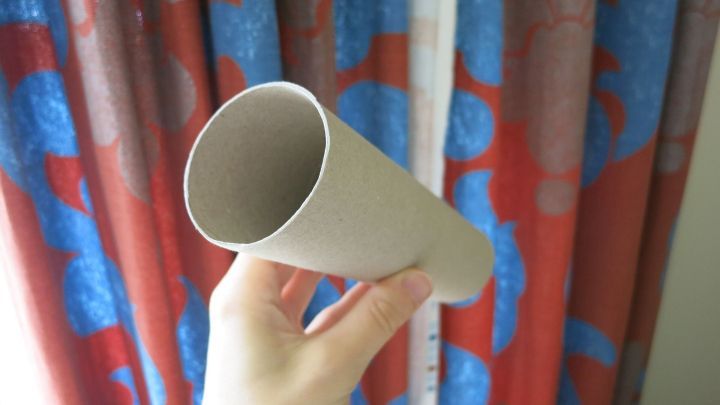 Eine Hand h&auml;lt ein leeres Toilettenpapierrohr, das auf bunte Vorh&auml;nge zeigt, die mit roten und blauen Mustern gestaltet sind.