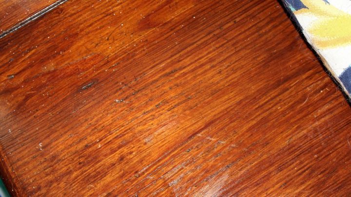 Eine dunkle Holzoberfl&auml;che zeigt Kratzer, die mit Fernet Branca behandelt werden, um Sch&auml;den zu reparieren.