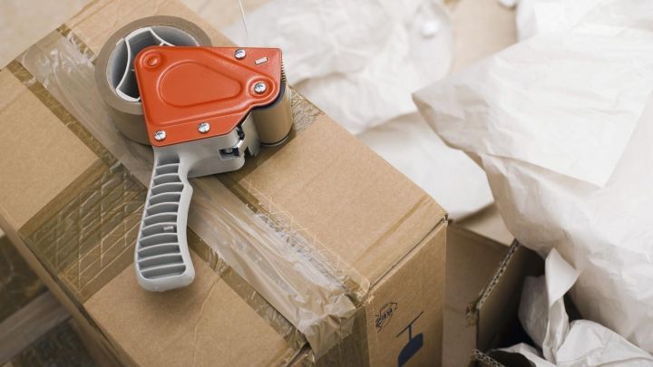 Abroller liegt auf einem zugeklebten Karton, umgeben von zerkn&uuml;lltem Papier, im Kontext von Verpackung und Klebereste.