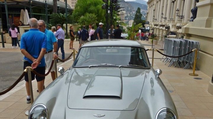 Ein gl&auml;nzendes, silbernes Auto steht auf dem Platz vor einem eleganten Geb&auml;ude, w&auml;hrend Passanten vorbeigehen.