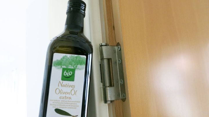Eine Flasche Pflanzen&ouml;l steht an einer T&uuml;r, w&auml;hrend das T&uuml;rscharnier geschmiert wird, um quietschende Ger&auml;usche zu verhindern.