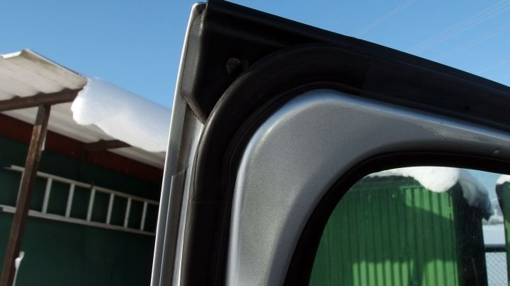 Ein ge&ouml;ffneter Autot&uuml;rrahmen zeigt frostige Bedingungen und Schnee auf dem Dach. Der Himmel ist klar und blau.