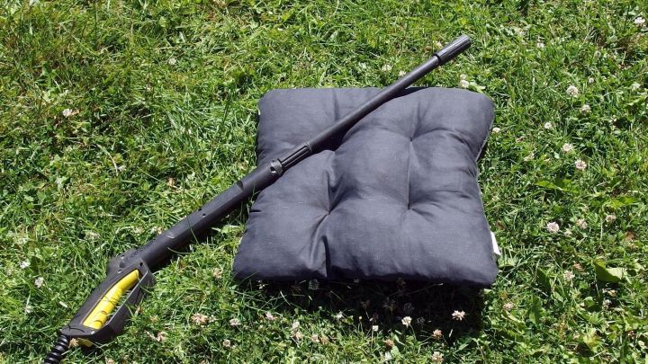 Ein Hochdruckreiniger liegt auf einem gepolsterten Autositz auf gr&uuml;nem Gras, bereit f&uuml;r die Autositzreinigung.