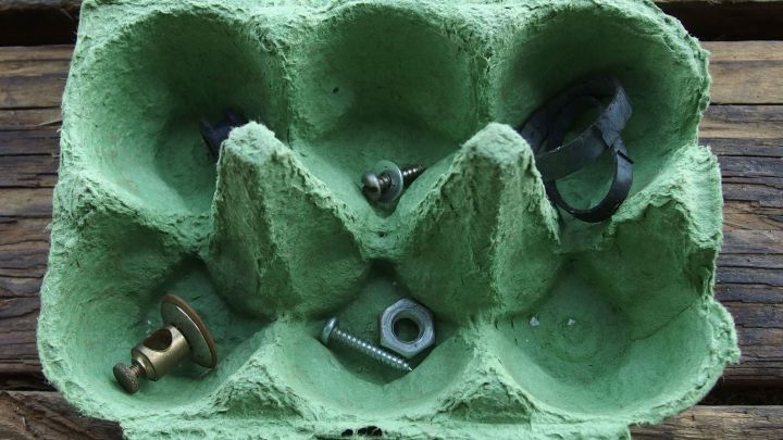 Eine Eierpappe h&auml;lt Metallteile organisiert, w&auml;hrend eine Motorzerlegung im Werkstattumfeld stattfindet.