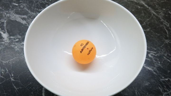 Ein Tablett mit einem eingedellten Tischtennisball liegt in einer wei&szlig;en Sch&uuml;ssel auf einer dunklen Oberfl&auml;che.