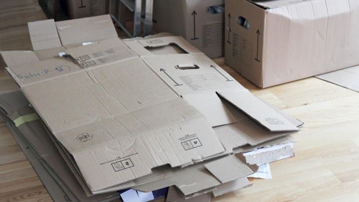 Umzugskisten liegen flach auf einem Holzboden, umgeben von zusammengebauten Kartons, die f&uuml;r den Umzug bereitstehen.