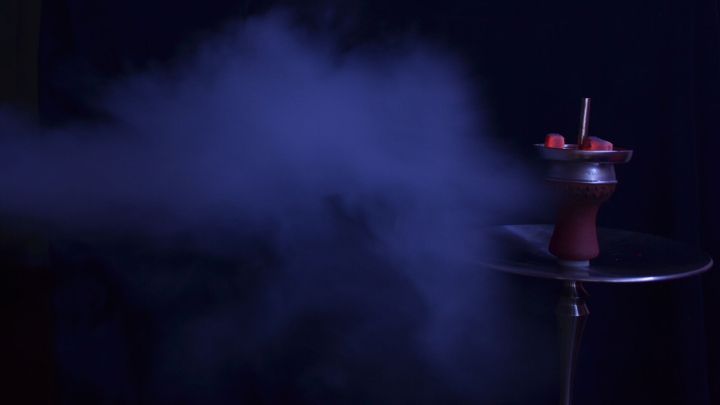 Eine Wasserpfeife erzeugt dichten Rauch, w&auml;hrend sie in einem dunklen Raum auf einem Tisch steht.