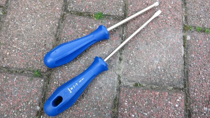 Zwei blaue Schraubenzieher liegen auf einem Pflastersteinboden, bereit zum Schrauben, ohne dass eine Schraube abf&auml;llt.