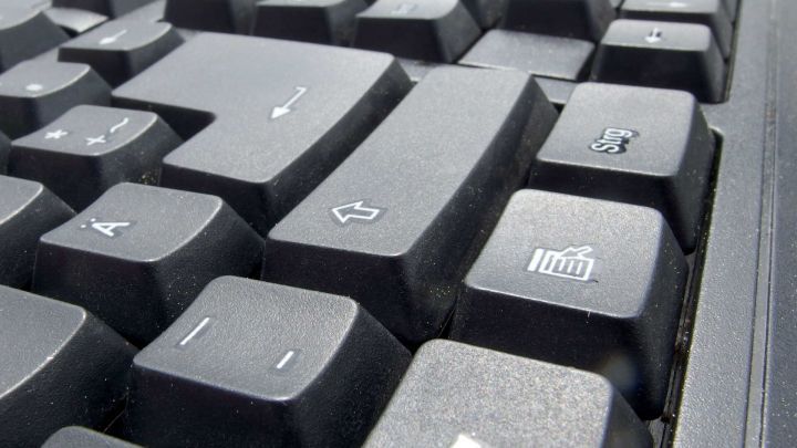 Ein Computerkeyboard liegt vor einem neutralen Hintergrund, w&auml;hrend Druckspray verwendet wird, um die Tasten zu reinigen.