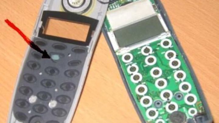 Handy mit abgenommener Tastatur wird repariert; zeigt Platine und Gummitasten, liegt auf einem Holztisch.