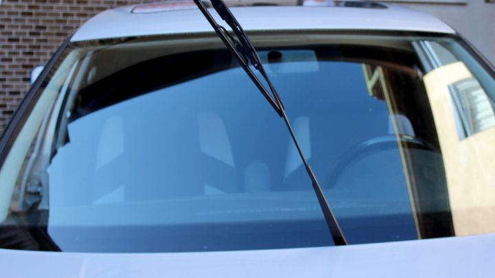 Eine Fahrzeug-Scheibe mit einem Wischer, bereit zum Einsatz, steht in einer st&auml;dtischen Umgebung, um Baumharz zu entfernen.