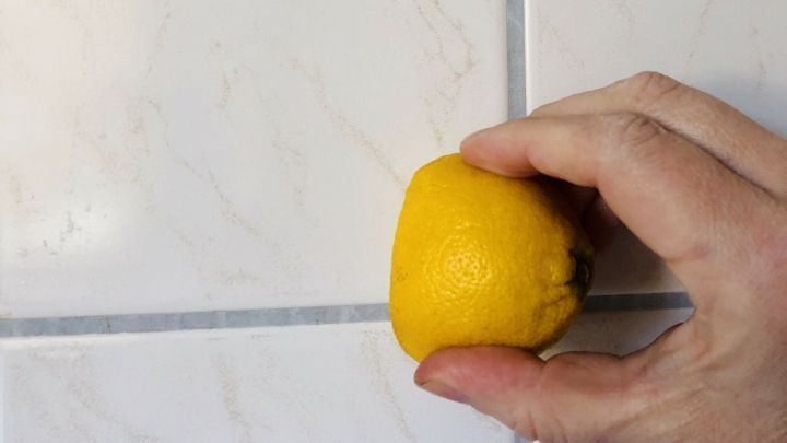 Eine Zitrone wird in der Hand gehalten und gegen eine fliesenartige Wand gedr&uuml;ckt, um Zementschleier zu entfernen.