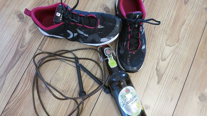 Sportliche Schuhe liegen neben einer Flasche Bier und einem Springseil auf einem Holzfu&szlig;boden, was einen Kater verdeutlicht.