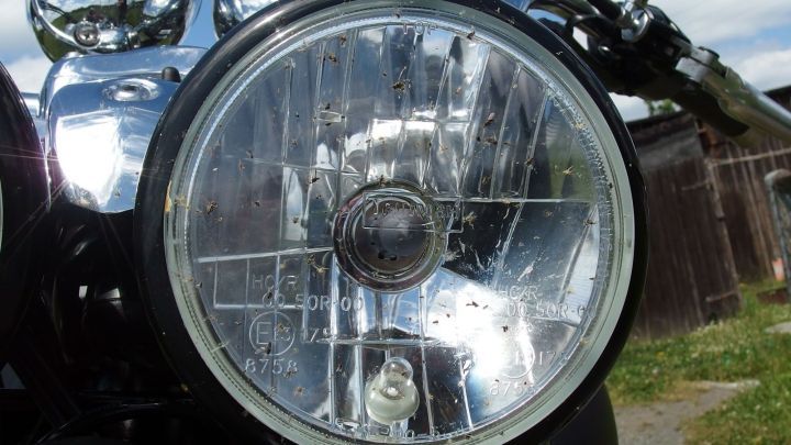 Ein Motorrad mit gl&auml;nzendem Scheinwerfer steht auf einer gr&uuml;nen Wiese, umgeben von Wolken und einem Holzzaun.