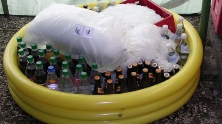 In einem gelben Planschbecken liegen zahlreiche Flaschen mit Getr&auml;nken, die mit Eis bedeckt sind, um sie zu k&uuml;hlen.