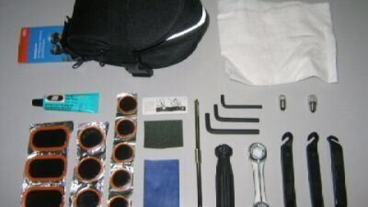 Fahrrad-Reparaturset liegt geordnet auf grauer Fl&auml;che; Schlauchflicken, Werkzeuge und eine schwarze Tasche sind ersichtlich.