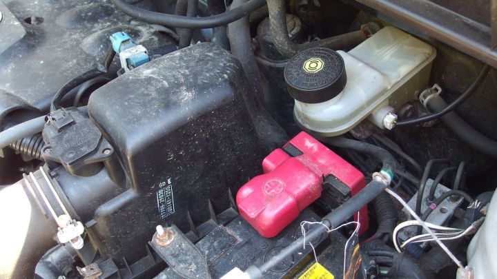 Ein Fahrzeugmotor mit einer roten Batterieabdeckung und einer Bremsfl&uuml;ssigkeitsbeh&auml;lter, umgeben von Kabeln und Komponenten.