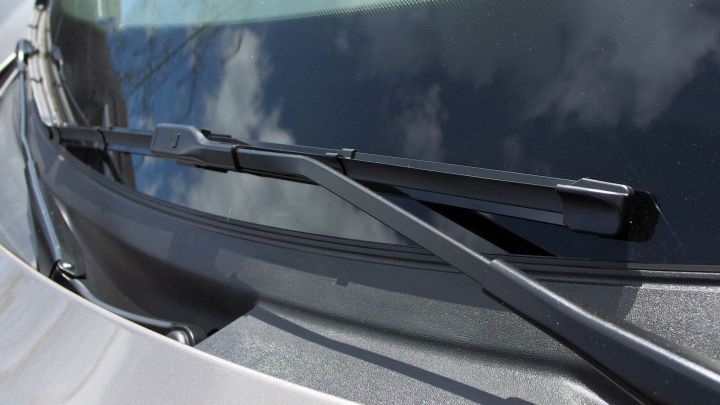 Scheibenwischer reinigen die Windschutzscheibe und entfernen Wasser, w&auml;hrend der Himmel reflektiert wird.