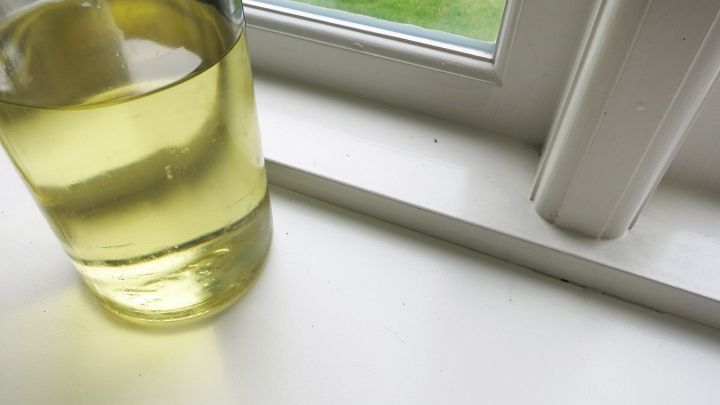Ein Glas mit Speise&ouml;l steht neben einem wei&szlig;en Fensterrahmen, wo es verwendet wird, um wei&szlig;e Fugen zu reinigen.