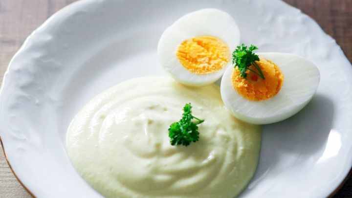 Eine cremige Senfso&szlig;e liegt auf einem wei&szlig;en Teller, garniert mit zwei halbierten, gekochten Eiern und Petersilie.