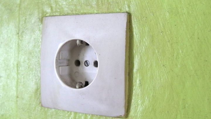 Eine wei&szlig;e Steckdose ist an einer hellgr&uuml;nen Wand montiert, bereit zum &Uuml;berpr&uuml;fen beim Tapezieren.