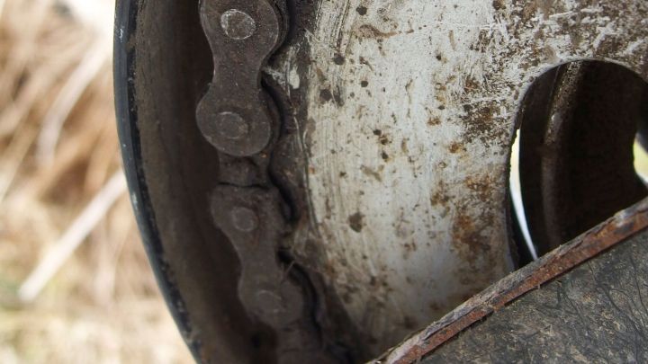 Eine verschmutzte Kette an einem Rad dreht sich schwerf&auml;llig in einer staubigen Umgebung, &uuml;berzogen mit schwarzem Fett.