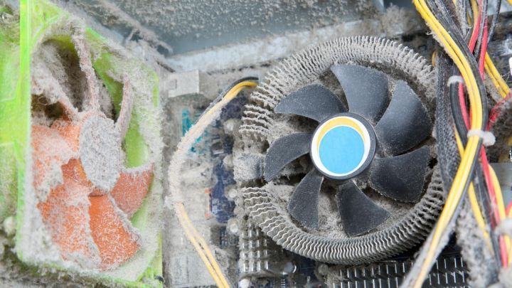 Ein PC-L&uuml;fter ist stark verstaubt und dreht sich, w&auml;hrend er in einem Computergeh&auml;use steht. Staubpartikel sind sichtbar.