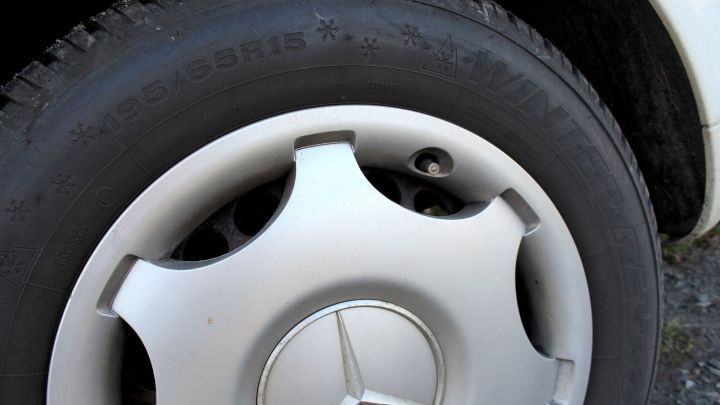 Ein silberner Alufelgen eines Mercedes auf einem Reifen, der in einem Außenbereich steht, wirkt leicht verschmutzt.