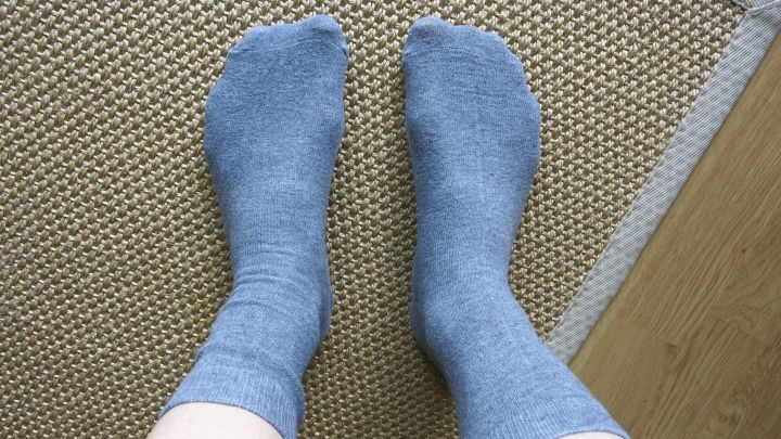 Graue Socken liegen auf einem Bodenbelag, die F&uuml;&szlig;e sind entspannt nebeneinander positioniert.