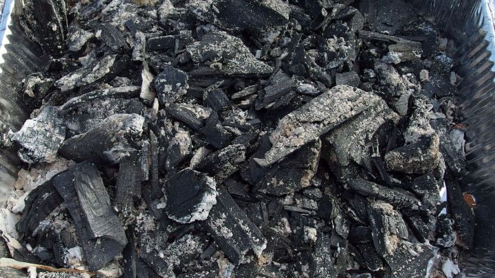 Ein feuchter Grill mit Resten von verbrannten Kohlen und Asche liegt in einer Aluminiumfolie im Freien.