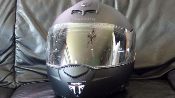 Ein Motorradhelm steht auf einem Lederstuhl, versehen mit Fliegenresten und reflektierender Visieroberfl&auml;che.