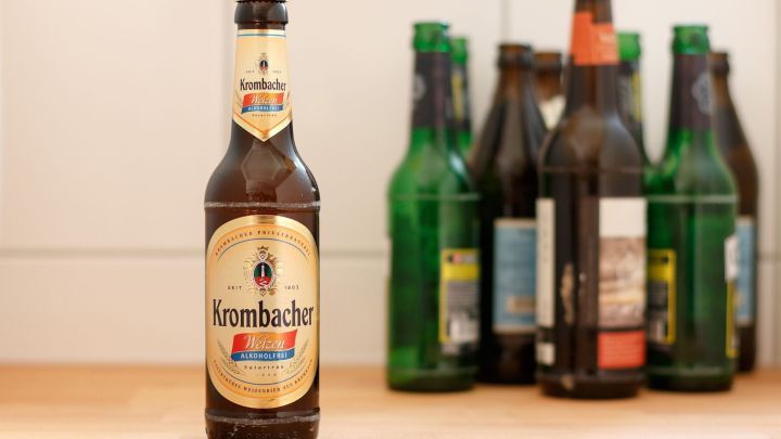 Eine Flasche alkoholfreies Bier steht auf einem Holztisch, umgeben von leeren, gr&uuml;nen und braunen Bierflaschen.